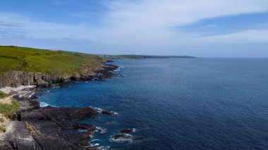 Güneşli bir bahar gününde Atlantik Okyanusu 'ndaki yeşil tepeler. Deniz kıyısında mavi gökyüzü. İrlanda kıyısı, West Cork. Hava fotoğrafı. Drone bakış açısı.