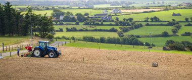 County Cork, İrlanda, 20 Ağustos 2022. Bir yaz günü İrlanda 'da mavi bir traktör sürülen bir tarlayı eker. Bir çiftlikte tarım işi.