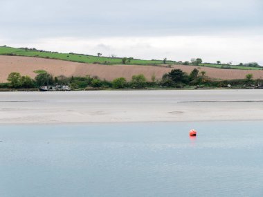 Clonakilty Körfezi 'nin alçak gelgit manzarası. Küçük bir turuncu şamandıra sakin bir su yüzeyinde tutulur..