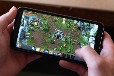 County Cork, İrlanda, 31 Temmuz 2022. Cep telefonu açık tenli bir adamın elinde, yakın plan. Mobil MMORPG Savaş Mızrağı Çevrimiçi oynatma süreci, resimsel yazı tipi.