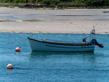 Güneşli bir bahar gününde küçük bir tekne demir atar. Mavi deniz suyunda tekne