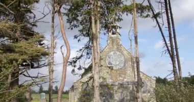 Darrara 'da 19. yüzyıldan kalma taştan bir kilisenin önündeki uzun kozalaklı ağaçlar. Bulutlu bir akşamda Hıristiyan kilisesi. Sacred Heart Roman Katolik Kilisesi (1897 'de inşa edildi), video.