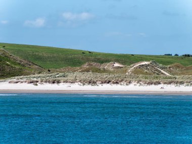 A sea under a clear blue sky. Sandy beach on the Atlantic Ocean. Seaside Irish landscape on a sunny spring day. Hilly coast.
