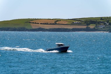 A small motor boat is sailing on the blue sea near the picturesque shores of Ireland. Seaside landscape on a sunny spring day.