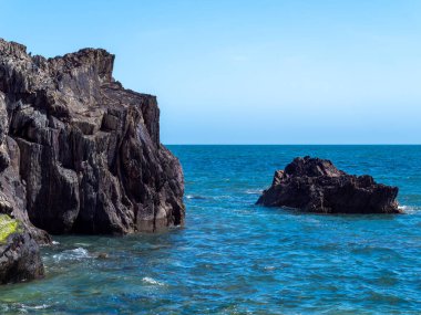 A huge stone rock among the blue sea waters. Seaside landscape, rocky mountain beside body of water.