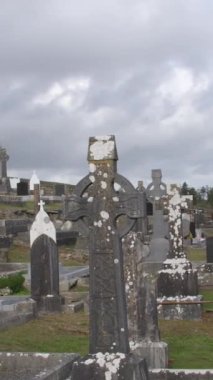 Stone tombstones and Celtic crosses in the Catholic cemetery. Overcast cloudy sky over a Christian cemetery in Ireland. Vertical.
