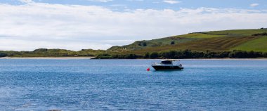 County Cork, Ireland, August 21, 2022. One small fishing boat on a calm water surface near the hilly Irish coast on a sunny summer day.