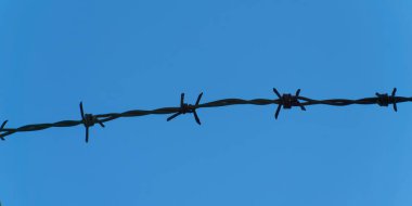 Metal barb wire on a background of clear blue sky, close-up. Black barb wire under blue sky, macro.