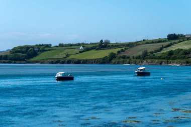 Two small boats are anchored in Clonakilty Bay on a sunny spring day. Beautiful Irish seaside landscape. Clear sky and blue water, boats on blue sea.