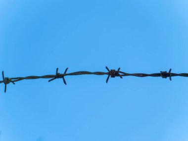 Metal barb wire on a background of blue sky, close-up. Black barb wire under blue sky, macro.