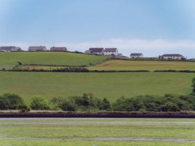 A houses on a hill under a blue sky on a summer day. A small Irish village. The countryside in Ireland. Green grass field