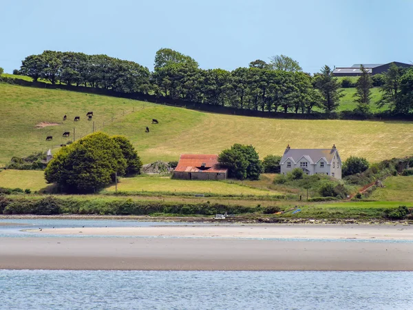 A farm, house on the green hilly shore of Clonakilty Bay. Rural Irish landscape. The picturesque nature of Ireland in summer, house near green trees and body of water.