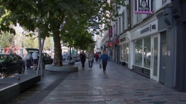 Cork, İrlanda, 30 Eylül 2022. Cork sakinleri bir sonbahar sabahı şehrin sokaklarından birinde yürüyorlar. İrlanda 'da şehir hayatı. Sokaktaki insanlar. video.