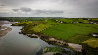 Green fields on the Irish hills, top view. The countryside of Ireland on a cloudy day. The coast of Clonakilty Bay at low tide. Green grass field under cloudy sky