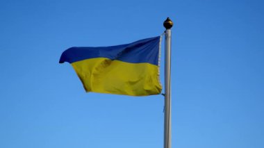 The blue and yellow Ukrainian flag is waving in the wind against a clear sky.