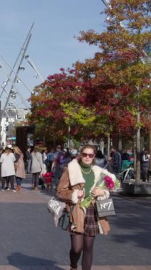 Cork, Ireland, September 30, 2022. A young girl with flowers walks down the street of a European city. Passers-by on the street on a autumn morning. Townspeople in an Irish town. Vertical video.
