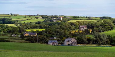 A small European village among green fields and trees. Farmhouses in Ireland. Picturesque agricultural landscape. Green fields under a blue sky, houses on green grass field.