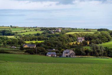 A European village among green fields and trees. Farmhouses in Ireland. Picturesque agricultural landscape. Green fields under a blue sky, houses on green grass field.