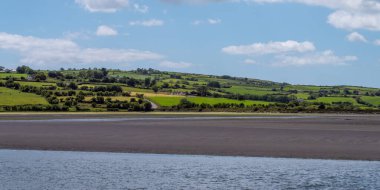 Gökyüzünde beyaz bulutlar, kırsal kesimde. Yazın yeşil tepeler. İrlanda kırsalı, County Cork. Beyaz bulutların ve gökyüzünün altında yeşil alan