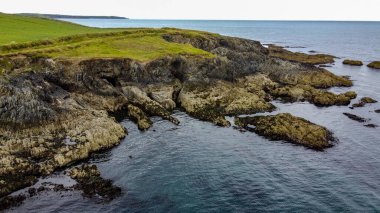 İrlanda 'nın Atlantik kıyısında kayalık bir pelerin. Deniz manzarası. Suyun yanında yeşil çimen tarlası