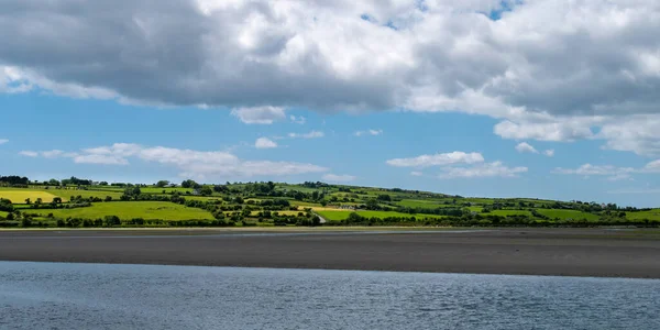 丘の上のアイルランドの田舎の空に白い積雲 素敵な夏の日に緑の丘 アイルランドの田舎 コーク州 白い雲と空の下の水の体の近くの緑の草原 — ストック写真