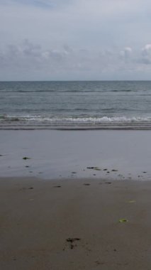 Üzerinde bulut benekli gökyüzü olan sakin ve pitoresk bir Atlantik su manzarası ve daha önce uzanan huzurlu bir kumsal. Dikey video.