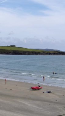 County Cork, İrlanda, 29 Ağustos 2022. Ünlü bir İrlanda plajı olan Inchydoney 'in kumsalında kırmızı plastik bir cankurtaran botu vardır. Hava güneşli ve aydınlık. Dikey video.