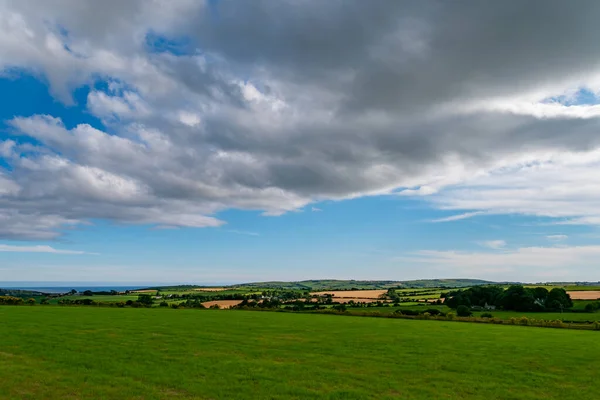 A grey cumulus cloud in the sky over the Irish countryside in summer. Irish landscape. Green farm fields. Green grass field under blue sky and white clouds