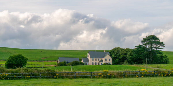 A large farmhouse among the green fields of Ireland. Cloudy sky over green pastures. Irish countryside landscape. house on green grass field under white clouds