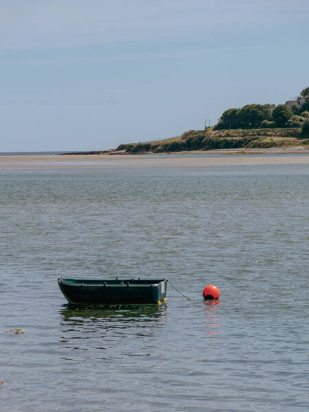 One small single-person plastic boat is anchored near the shore in Ireland on a sunny summer day. Seaside Irish landscape. boat, sea