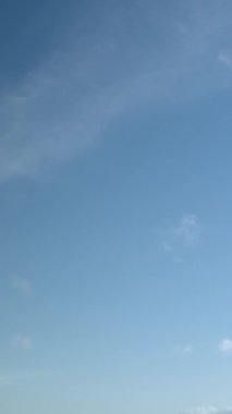 Pofuduk bulutlar açık bir gökyüzünde kıyıya vuruyor. Dikey video.