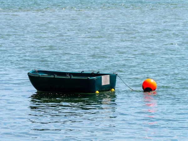 A small single-person plastic boat on the surface of the water. Orange buoy on the water near the boat.  boat on body of water