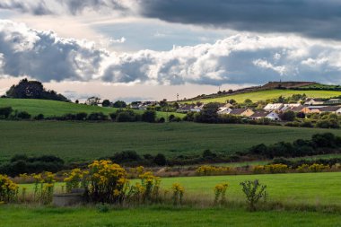 Akşamları gökyüzü kümülüs bulutlarıyla bir İrlanda köyünün üzerinde. County Cork 'taki İrlanda yerleşimi, manzara. Avrupa kırsal kesimi, kırsal kesim. Bulutlu gökyüzünün altındaki yeşil çimen tarlası