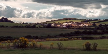 Akşamları gökyüzü kümülüs bulutlarıyla bir İrlanda köyünün üzerinde. County Cork 'taki İrlanda yerleşimi, manzara. Avrupa kırsal kesimi, kırsal kesim. Gökyüzünün altındaki yeşil alan