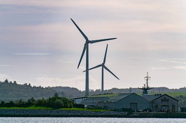 İrlanda 'nın güneyinde rüzgar jeneratörleri, manzara. Ringaskiddy, County Cork 'ta iki rüzgar türbini bulundu. Bulutlu bulutlu gökyüzü. Gökyüzünün altındaki rüzgar türbini