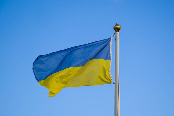 Один украинский синий и желтый флаг висит на флагштоке на ясном небе. Флаг Украины, размахивающий ветром против голубого неба.