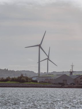 İrlanda 'nın güneyinde rüzgar jeneratörleri, manzara. Ringaskiddy, County Cork 'ta iki rüzgar türbini bulundu. Bulutlu bulutlu gökyüzü. Bulutlu gökyüzünün altında rüzgar türbini