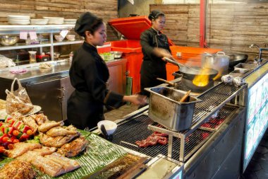 Siem Reap, Kamboçya, Aralık 2018. Siyah elbiseli iki kız, Asya 'da bir gece şehrindeki bir kafede yemek pişiriyor. Asya mutfağı, sokak yemekleri..