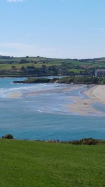 Inchydoney 'deki büyüleyici İrlanda plajının panoramik bir görüntüsü, açık mavi su güneşli gökyüzünü yansıtıyor. Dikey video.