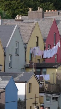 İrlanda 'nın Cobh kasabasındaki renkli evlerin arka planında çamaşırları kurutmak. Dikey video.