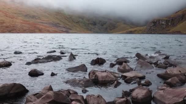 海岸を点在する低張りの雲と険しい石を持つセレンアイルランドの山岳湖 — ストック動画