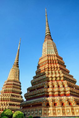 Görüntü, Tayland 'da güneşin sıcacık ışığıyla aydınlatılan renkli kiremitler ve desenlerle süslenmiş tapınak kulelerini tasvir ediyor..