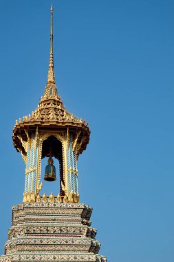 Altın çatılı ve renkli detaylarıyla süslü bir Tayland tapınağı çan kulesi açık mavi gökyüzüne karşı duruyor..