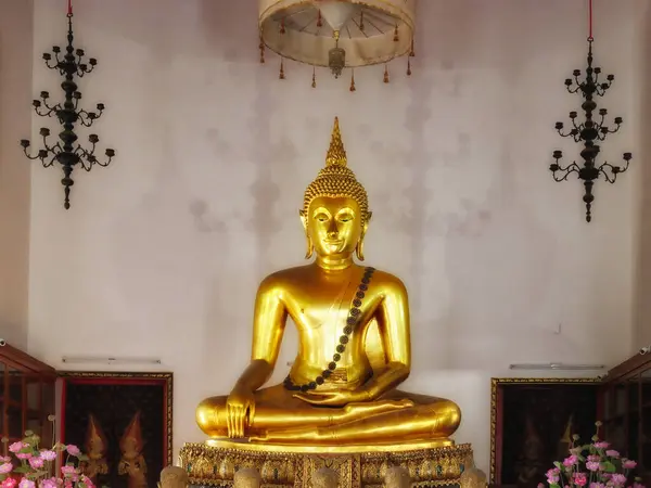 寺院に金像が置かれている 像はイメージの中心にあり 蓮の位置に座っています 彫像の両側に花瓶にピンクの花がある — ストック写真