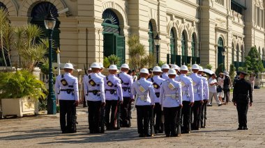 Bangkok, Tayland, 27 Aralık 2018. Beyaz miğferli ve siyah pantolonlu bir grup üniformalı adam ellerinde süngülerle, yeşil panjurlu beyaz bir binanın önünde sıra bekliyor..