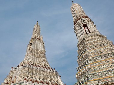 Tayland 'da iki tapınak kulesi. Kuleler uzun ve süslü, karmaşık desenleri ve tasarımları var. Kuleler renkli aksanlı beyaz malzemelerden yapılmıştır. Gökyüzü mavi, bulutlar.