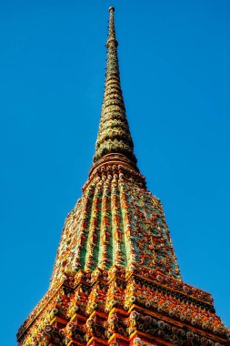 Fotoğraf, Tayland 'daki süslü tapınak kulelerini gösteriyor. Renkli kiremitler ve desenlerle sıralanmış. Güneşin sıcacık ışığında parlıyorlar..