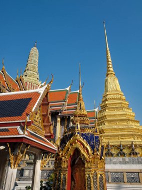 Büyüleyici düşük açılı perspektif tüm ihtişamıyla bir Tayland tapınağını yakalar: göz kamaştırıcı kırmızı çatılar, parıldayan altın detaylar, ve kusursuz mavi gökyüzü tarafından çerçevelenmiş görkemli beyaz bir zirve..