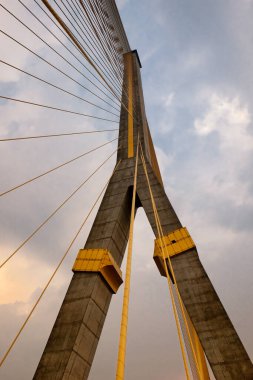 Beton sütunlar ve çelik kablolarla yükselen asma köprü bulutlu bir gökyüzüne karşı duruyor..
