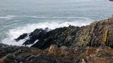 Kayalık bir sahil şeridi, sivri kayaları okyanus dalgalarının amansız saldırısına karşı dimdik ayakta duruyor. Denizin koyu mavi tonu, dalgaların beyaz köpüğü. yakınlaştır